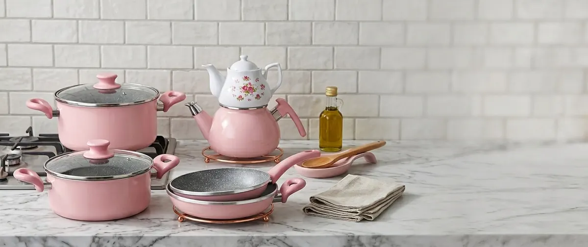 Pink EN GRANIT pots, pans and a teapot on a marble worktop